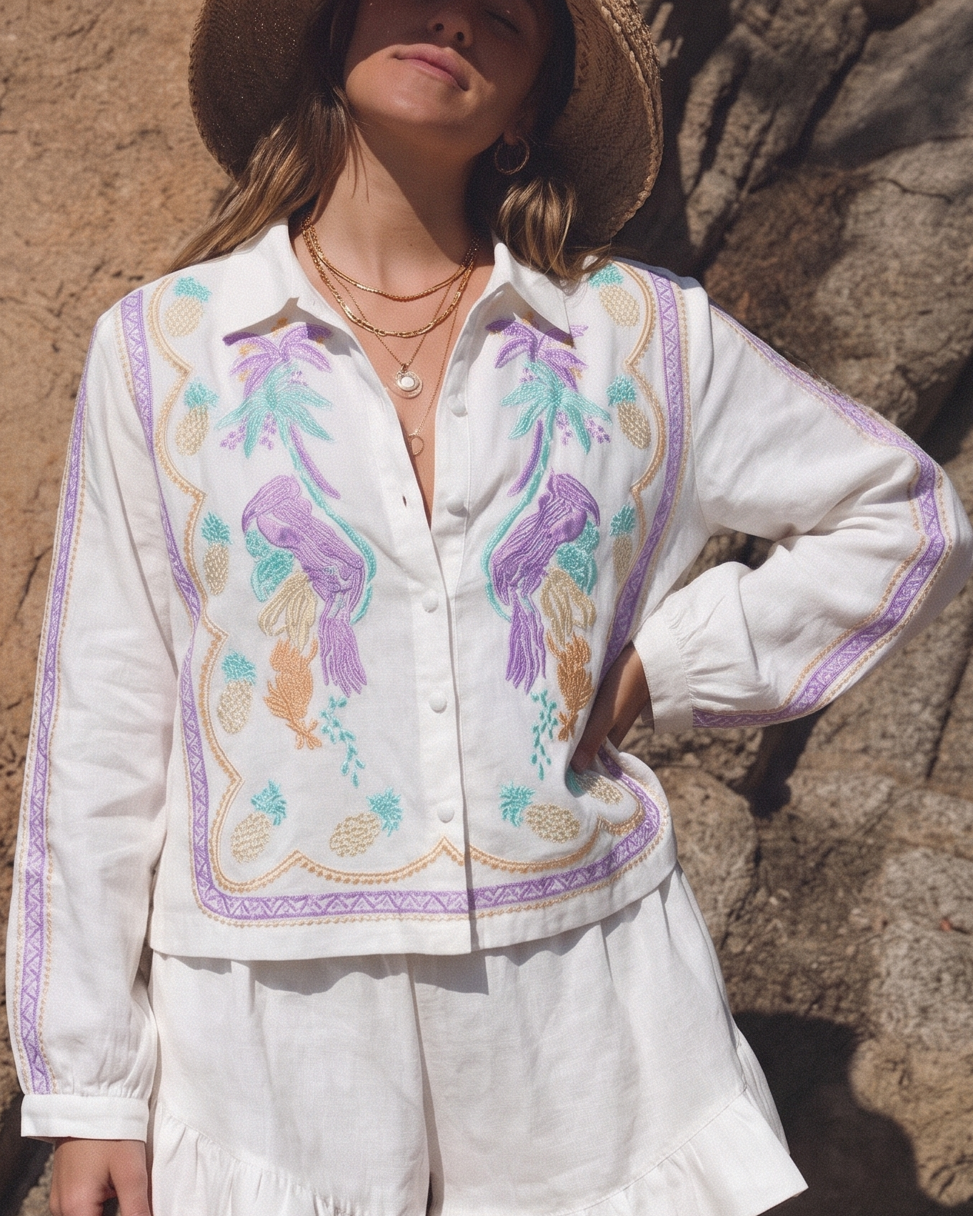 Woman wearing a white embroidered blouse and shorts against a rocky wall.
